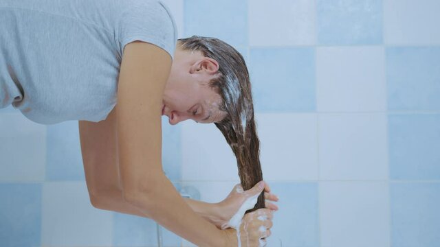 Young woman washes away the shampoo from her hair while. Concept of cleanliness of hair and body.