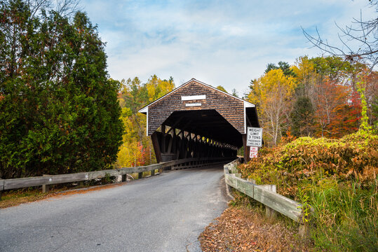 Historic wooden covered bridge with colourful autumnal trees in background on a partly cloudy day. Bath, NH, USA.