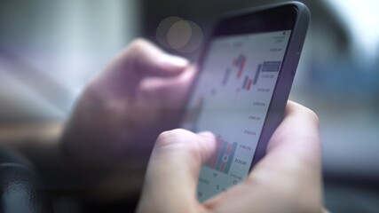 Hands with a mobile phone, checking stock market data. Smartphone with stock market graph on a touch screen device close up, blurred with bokeh effect