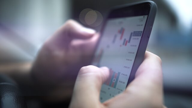 Hands with a mobile phone, checking stock market data. Smartphone with stock market graph on a touch screen device close up, blurred with bokeh effect