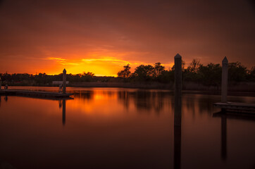 Fototapeta premium Sunset over a river, creating silhouette of docks and pilings, as well as trees.