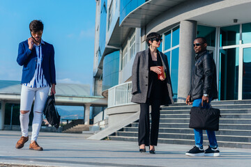 Two business colleagues discussing some reports outdoors while their young suited male colleague is talking on the phone