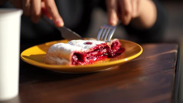 A woman cuts a cherry strudel with a knife. Homemade strudel with cherry close-up on a plate.