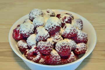 Ripe red raspberry berries, sprinkled with powdered sugar, in white cup