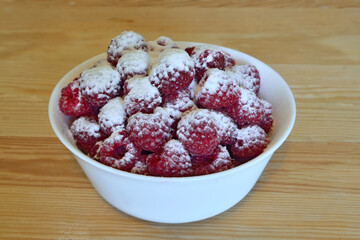 Ripe red raspberry berries, sprinkled with powdered sugar, in white cup