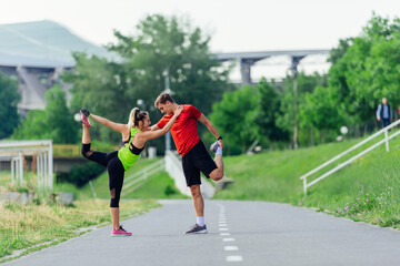 Fototapeta premium Young couple warming up and stretching together in a park before running