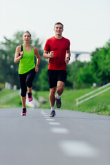 Young running couple jogging on an asphalt road in the park