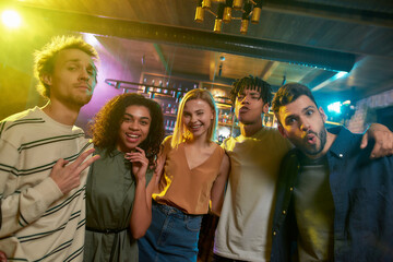Portrait of young men and women looking at camera and smiling. Multiracial group of friends hanging out at party in the bar