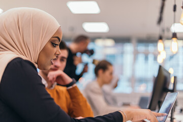 .Close-up portrait of a beautiful, charming, young woman with a hijab looking at her computer and...