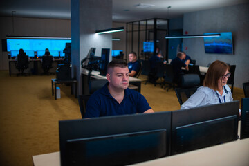 Group of Security data center operators (administrators) working in a group at a CCTV monitoring room while looking at multiple monitors ( computer screens)