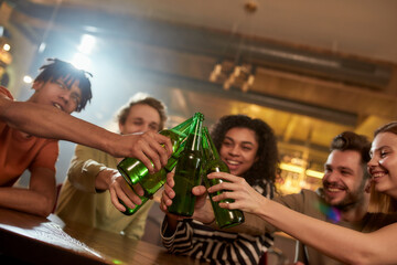 A group of happy friends in the bar clinking bottles while drinking beer together. People, leisure, friendship and entertainment concept