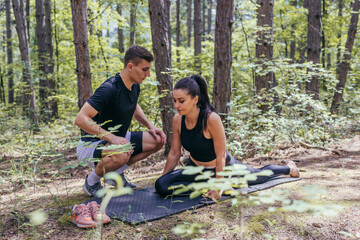 Naklejka na ściany i meble A beautiful young fitness couple is preparing for stretching before running in the forest.