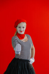 Fototapeta na wymiar Woman mime near a red wall in a red beret shows a sign with her hand.