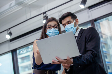 young business with face mask work plan in the office. Businessman and businesswoman using a laptop together while standing in front of office