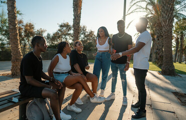 Group of young modern african black friends happily sitting together on the bench of the stairs in bright sunlight enjoying summer vacation