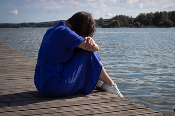 Sadness Woman Sitting by the River on pier. Empty place for text. Bad Day Concept.