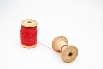 Two wooden spools of thread. One is full, the other almost empty, connected by a single thread. Togetherness as a concept, no people, without people