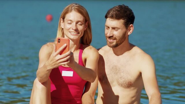 Close up portrait young man and woman is sitting on board use phone smiling chating talking surfboard soak water swimsuit freedom active close up slow motion