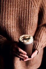 a girl in a brown sweater is holding a glass of coffee with cream