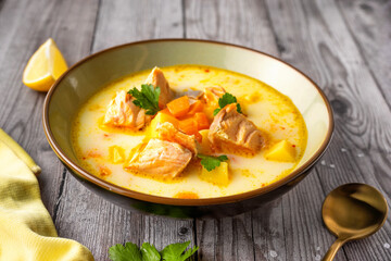 Side view of a plate with delicious bright salmon fish soup on gray wooden surface