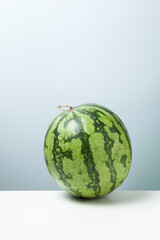 Whole striped watermelon on a white table. Light background, vertical orientation, copy space