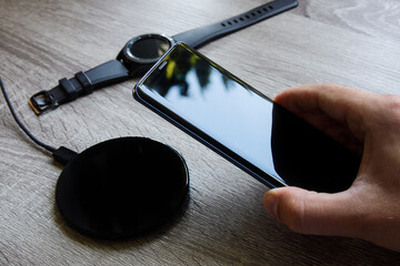 Smartphone held in the hand is placed on the wireless charger. Smart watch lying in the background