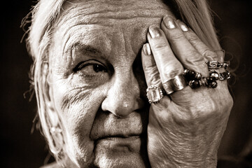 Portrait of an elderly woman with many wrinkles. The woman covers one eye with her hand.
