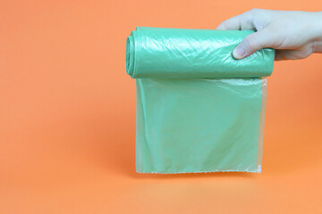 Plastic, green package in a female hand on an orange background. Copy space - concept of trash, waste, environmental care, recycling, ecological problems