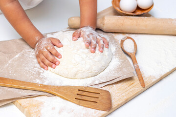 dough in flour kneading childrens hands, one kid, child helps parents in kitchen, concept of a happy childhood, household help, homework, food preparation
