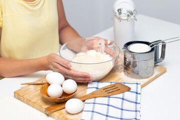 making dough for bread or homemade baked goods. ingredients on the table. female hands hold a mixer for mixing dough