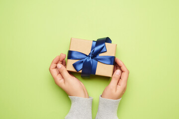 two female hands hold a gift paper box on a green background