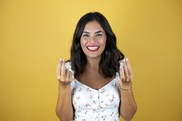 Beautiful woman over yellow background doing money gesture with hands, asking for salary payment,...