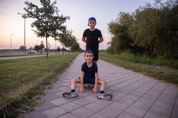 Cool 7 year old boys with skateboard on the street. Childhood. Summertime.