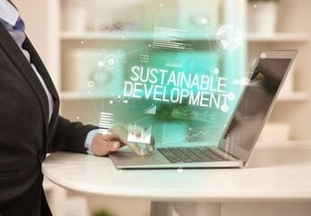 Side view of a business person working on laptop with SUSTAINABLE DEVELOPMENT inscription, modern business concept