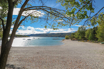 Beach on the lake of Sainte-Croix with blue melting water with forest mountains around, commune of Les Salles-sur-Verdon, Provence-Alpes-Côte d'Azur region, Alpes de Haute Provence, France