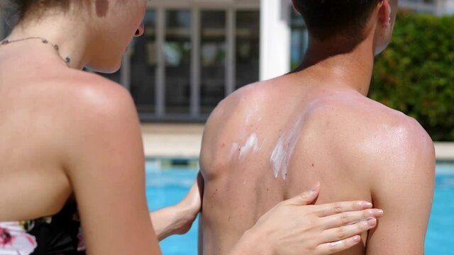 holiday, summer - young woman spreading sunscreen on her boyfriend's shoulders