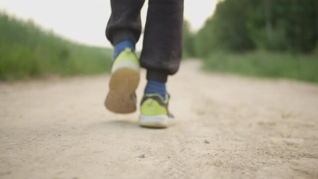 close-up of a boy's feet walking along a country road in dirty clothes