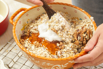 Woman making homemade granola in the kitchen. Serie of photos of all recipe's steps. Mixing all ingredients in the big bowl.