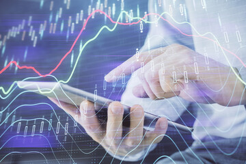 Double exposure of man's hands holding and using a digital device and forex graph drawing. Financial market concept.