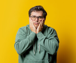 man with headache in green hoodie on yellow background