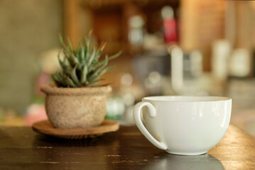 A white cup of coffee on wooden table in front of a coffee bar.