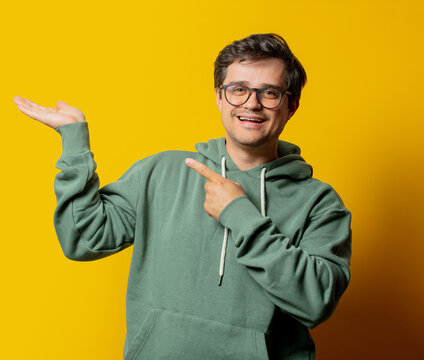 man show something in green hoodie on yellow background