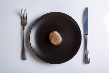 Raw one mushroom Suillus bovinus Jersey cow mushroom bovine bolete in a black plate and a knife and fork nearby on a white background top view. Horizontal orientation. High quality photo