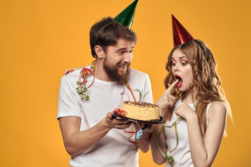 Man and woman birthday festive cake yellow background and caps on the headv