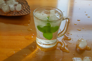 Ice water with fresh mint leaves close up on wood surface