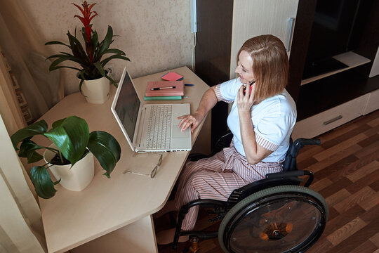 A female freelancer, disabled in a wheelchair, works remotely from home. Disabled woman talking on a cell phone.