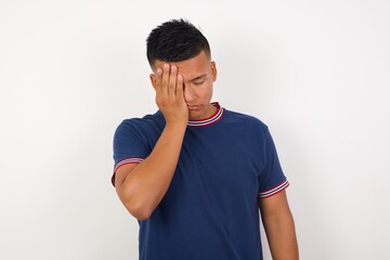 Tired overworked Young handsome hispanic man wearing casual t-shirt standing  has sleepy expression, gloomy look, covers face with hand, has eyes shut, gasps from tiredness, fatigue after party