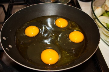 four chicken eggs being cooked in a round black pan