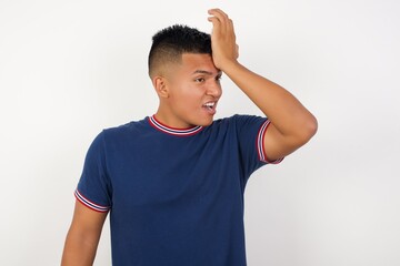 Young handsome hispanic man wearing casual t-shirt standing over white isolated background surprised with hand on head for mistake, remember error. Forgot, bad memory concept.