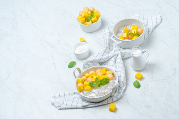The thai dessert food modern style : The homemade sago in coconut milk with topping is mango cut into squares and cantaloupe ball in the white bowl and placed on tablecloth plaid on the marble table.